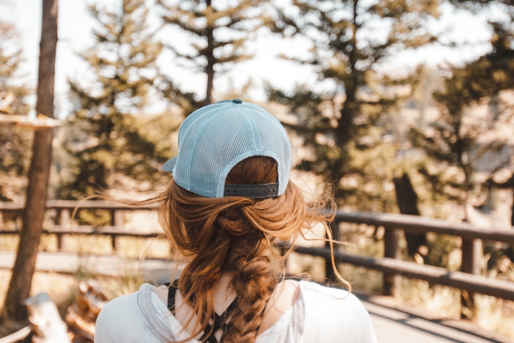 woman with blue trucker cap standing near brown wooden fence on road