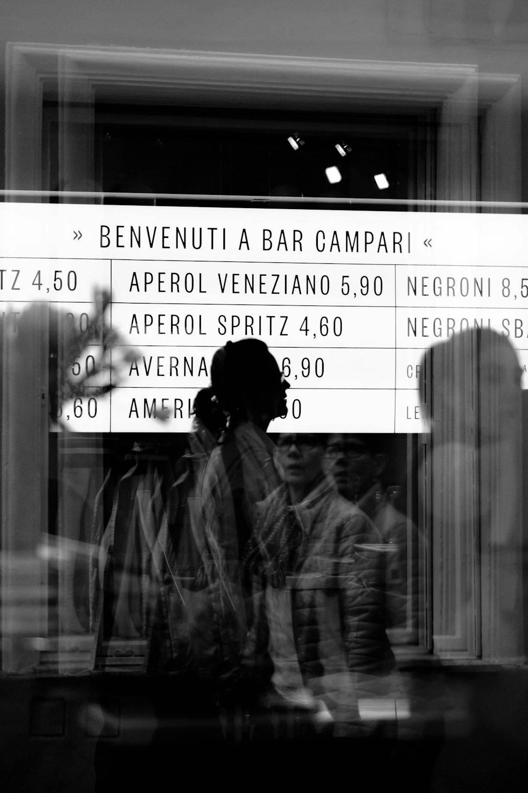 reflection of people from glass panel walking and passing signage in grayscale photography