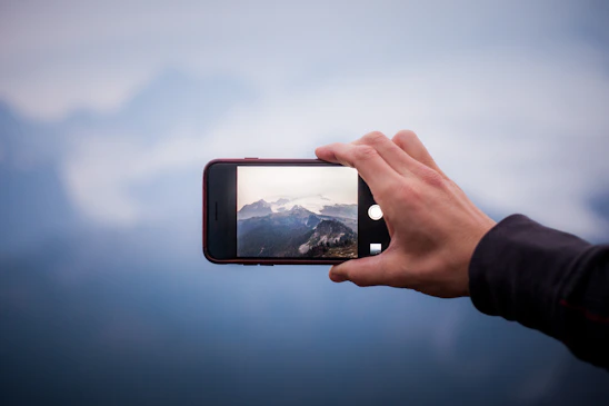 A vibrant photo of a travel influencer capturing a scenic mountain view with a tech gadget in hand.