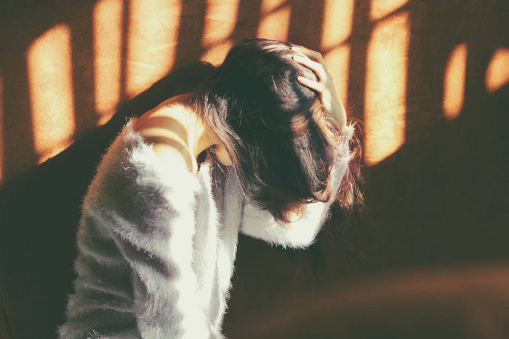 woman leans on wall in white fur jacket docking her head while holding it using her leaf hand