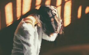 woman leans on wall in white fur jacket docking her head while holding it using her leaf hand
