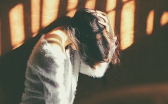 woman leans on wall in white fur jacket docking her head while holding it using her leaf hand