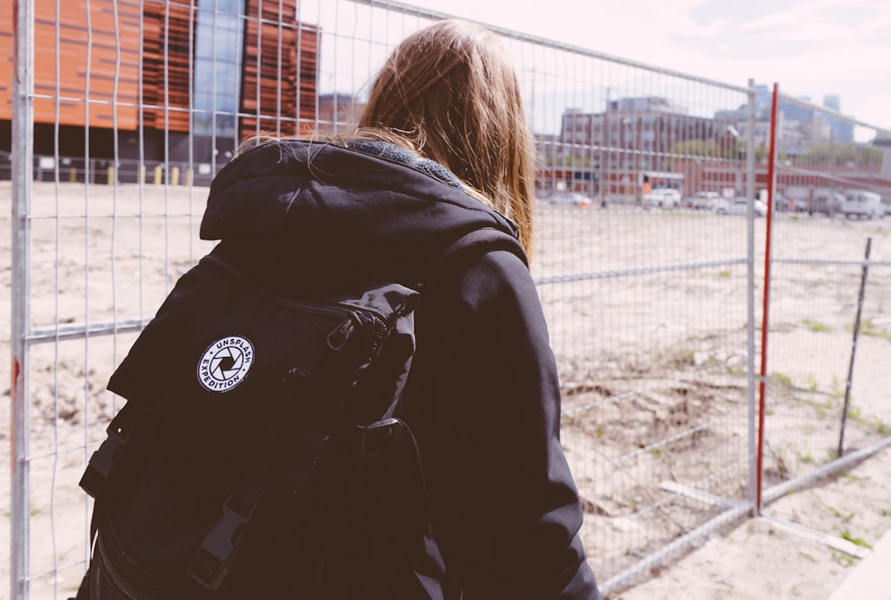 person wearing black jacket walking near fence