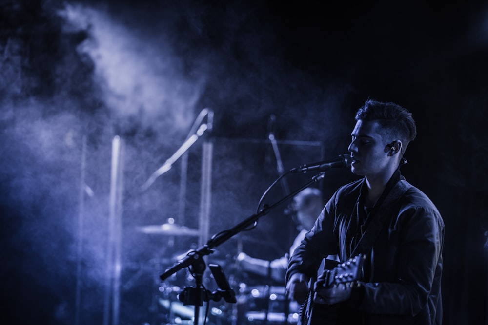 man playing acoustic guitar while singing on stage