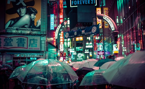 people holding umbrellas on a busy street at night lit by street lights and illuminated signs in Tokyo, Japan