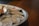 On a round tray, several shucked oysters are arranged with crushed ice. A small white dish containing red sauce and a wooden spoon accompanies the seafood on the tray.
