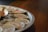 On a round tray, several shucked oysters are arranged with crushed ice. A small white dish containing red sauce and a wooden spoon accompanies the seafood on the tray.