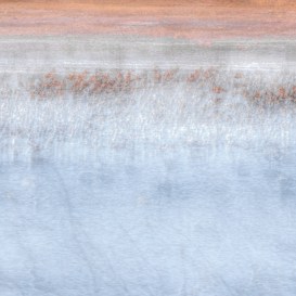 A serene and abstract landscape featuring a gradient of colors from earthy reds and browns at the top, transitioning to muted whites and blues below. The texture suggests reflections on a water surface, giving a calm and tranquil impression.
