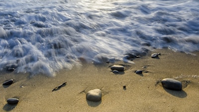 Delicate waves gently washing over smooth stones and scattered sea glass on the beach.