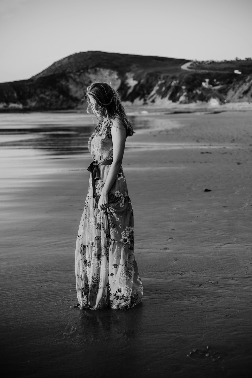 Frau im geblümten langen Kleid steht am Meeresufer
