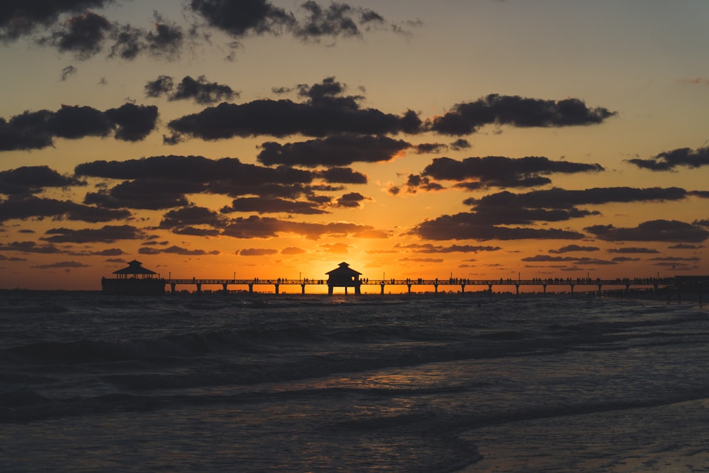 silhouette photo of dock with huts during golden hour