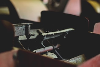 A close-up view of an old, rusted mechanical component likely part of an engine or machinery. The metal surfaces are covered in dust and exhibit signs of wear and tear.