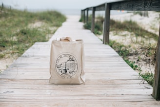 Close-up of a stylish tote bag with beach-themed patterns hanging on a wooden post.