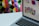A laptop displaying a colorful grid of app icons is set against a vivid, geometric patterned background. The laptop screen shows various colored circles and app logos, suggesting a focus on digital or graphic design.