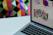 A friendly designer working on a laptop with colorful digital product icons floating around.