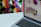 A laptop displaying a colorful grid of app icons is set against a vivid, geometric patterned background. The laptop screen shows various colored circles and app logos, suggesting a focus on digital or graphic design.