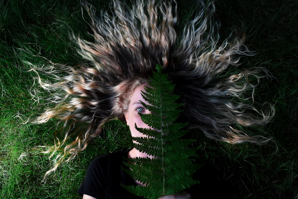 woman lying on grass and holding green leaf