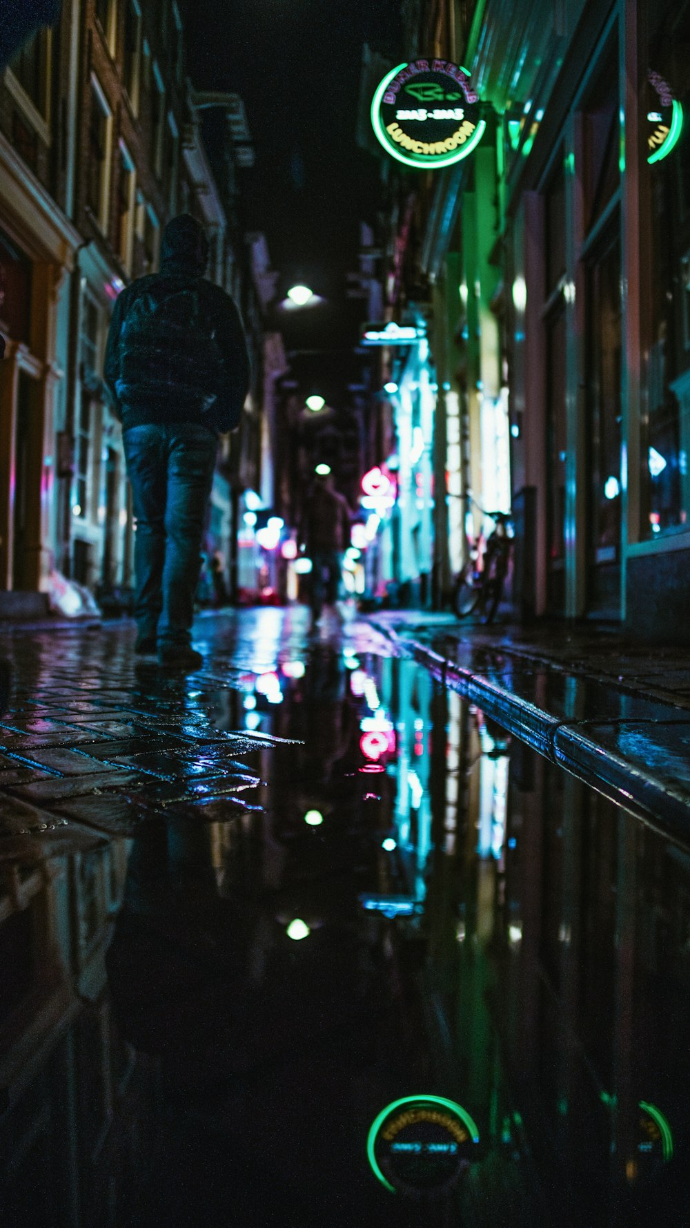 man wearing jacket walking between buildings during nighttime