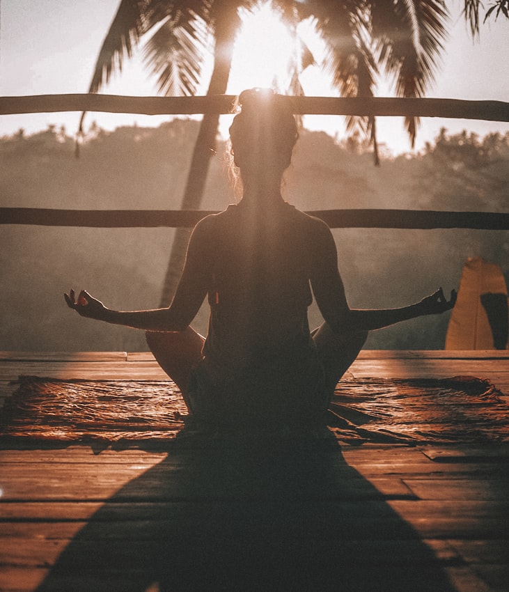 Woman meditating on dock overlooking sunset