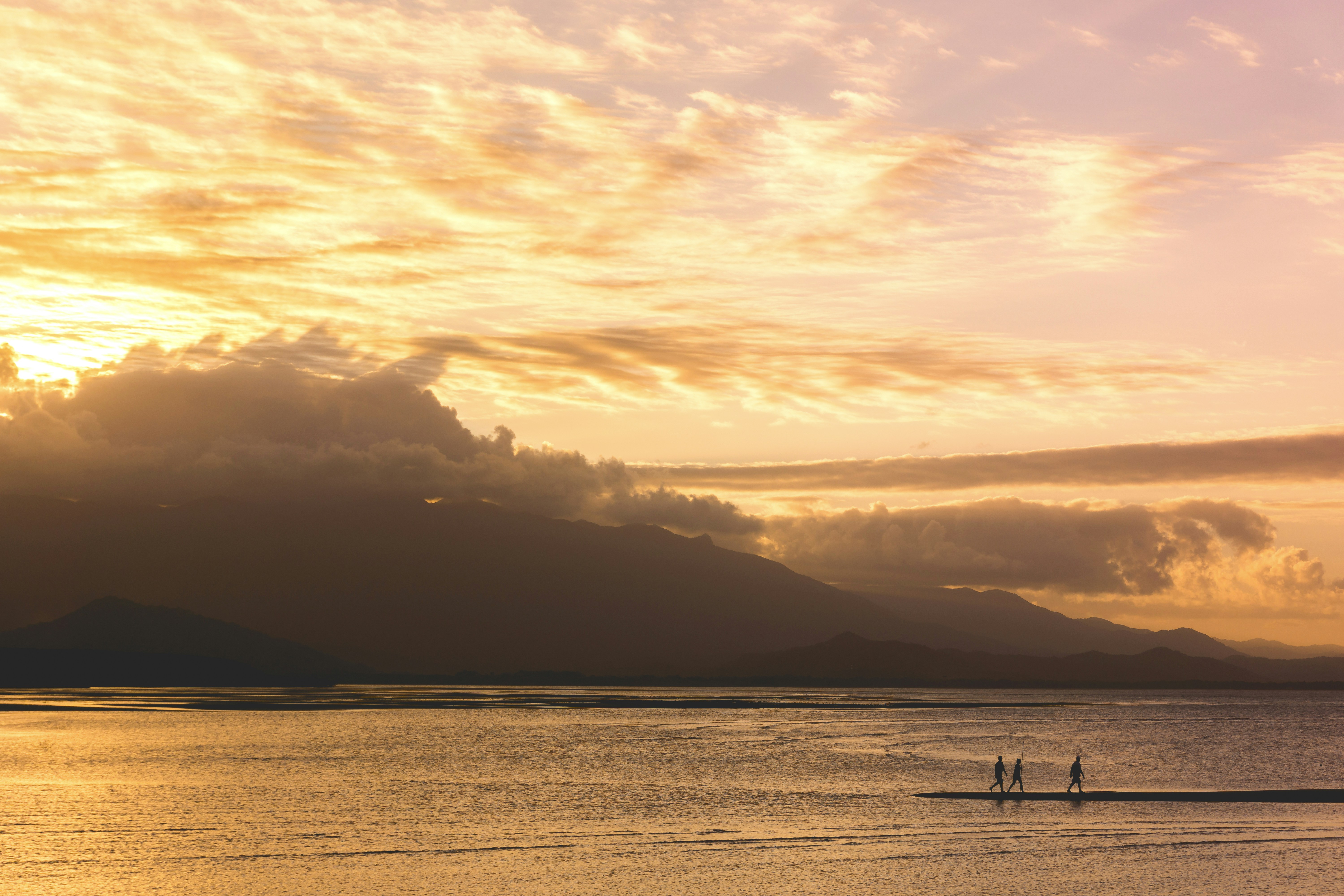 silhouette of three people walking on body of water during golden hour