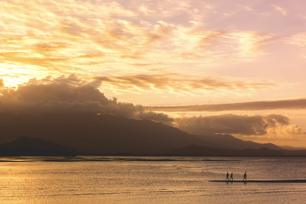 Silhouette von drei Menschen, die während der goldenen Stunde auf einem Gewässer spazieren gehen