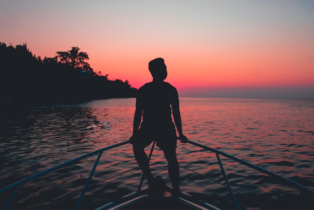 silhouette of a man sitting on fence of motorboat during golden hour