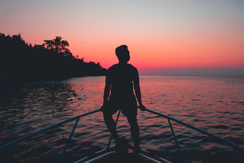 Silhouette eines Mannes, der während der goldenen Stunde auf dem Zaun eines Motorboots sitzt