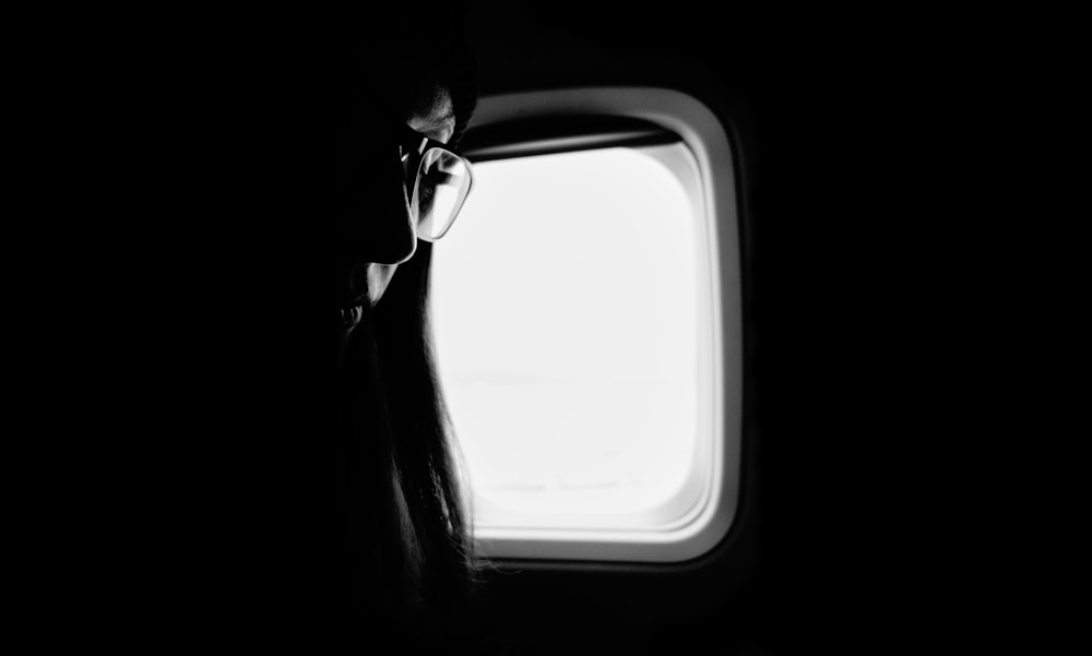 ein Schwarz-Weiß-Foto einer Person, die aus einem Flugzeugfenster schaut