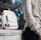 woman wearing beige and red floral top leaning on gray concrete slab with white leather bag ontop