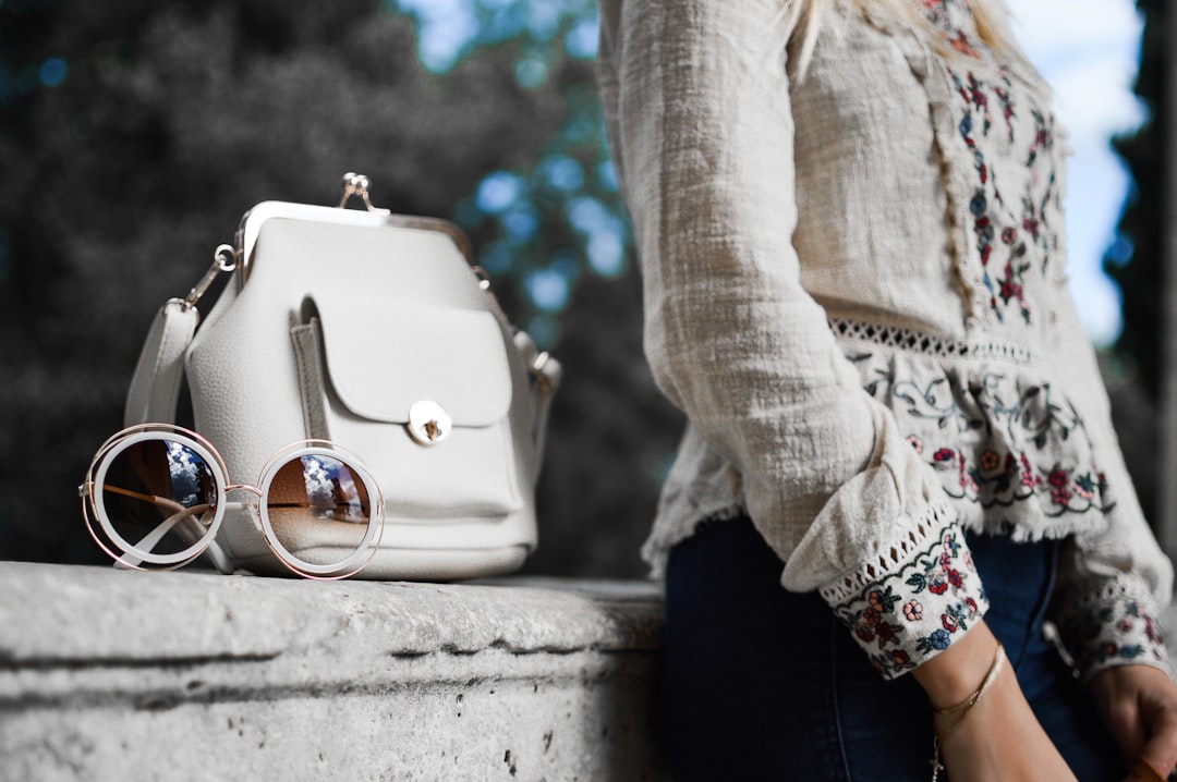 woman wearing beige and red floral top leaning on gray concrete slab with white leather bag ontop, Even though living in Sunny Greece, while September coming to its end, we can feel the Autumn coming. Clothes getting longer, jeans and shirts are now with long sleeves. Nevertheless, this doesn’t discourage Tamara to prepare extraordinary looks which we Shoot for her Fashion blog. It is these looks combined with a lovely pose of her and some proper light and focus, that make a capture like this possible.<p></figure>From: https://shinyhoney.com/blog-outfits-dragonfly-girl.html