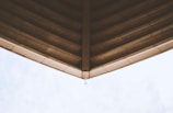 The image captures the underside of a large roof structure with a pointed design. The roof appears to be made of concrete or a similar material, with visible beams and lines running parallel to the point. The sky is visible in the background, offering a contrast to the architectural element.