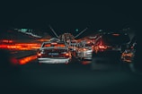 A congested traffic scene in a tunnel with numerous vehicles, including taxis and cars, lined up and emitting red brake lights that illuminate the sides of the tunnel. The atmosphere is dimly lit, with a focus on the glowing lights reflecting off the wet road and tunnel walls.