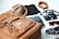 Various travel essentials are organized on a flat surface, including a tan backpack, a brown hat, a black notebook, a plaid scarf, a bandana, a vintage camera, sunglasses, and a patterned sneaker.