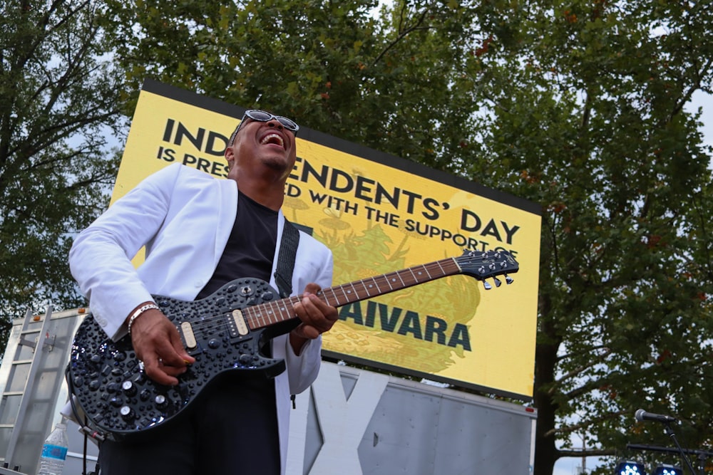 man standing on stage while playing black electric guitar