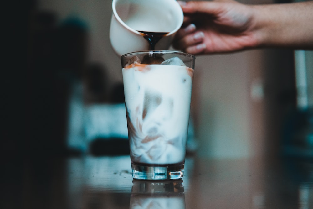 person pouring coffee on glass of milk