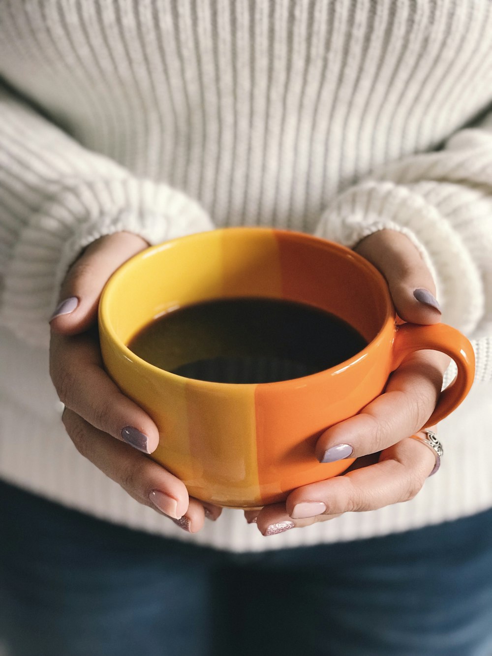 Ragazza che tiene una tazza arancione piena di liquido di colore marrone scuro