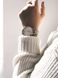 Close-up of a woman's wrist wearing a sleek auratime watch with a soft pink strap and gold face, bathed in warm natural light.
