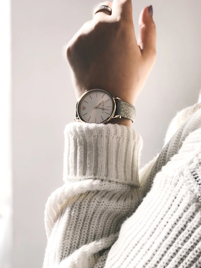 Close-up of a woman's wrist wearing a sleek auratime watch with a soft pink strap and gold face, bathed in warm natural light.