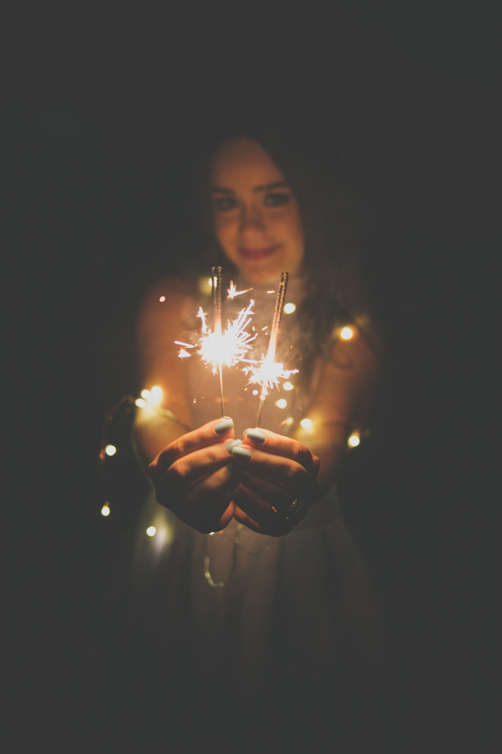 woman carrying two lighted sparklers against black background