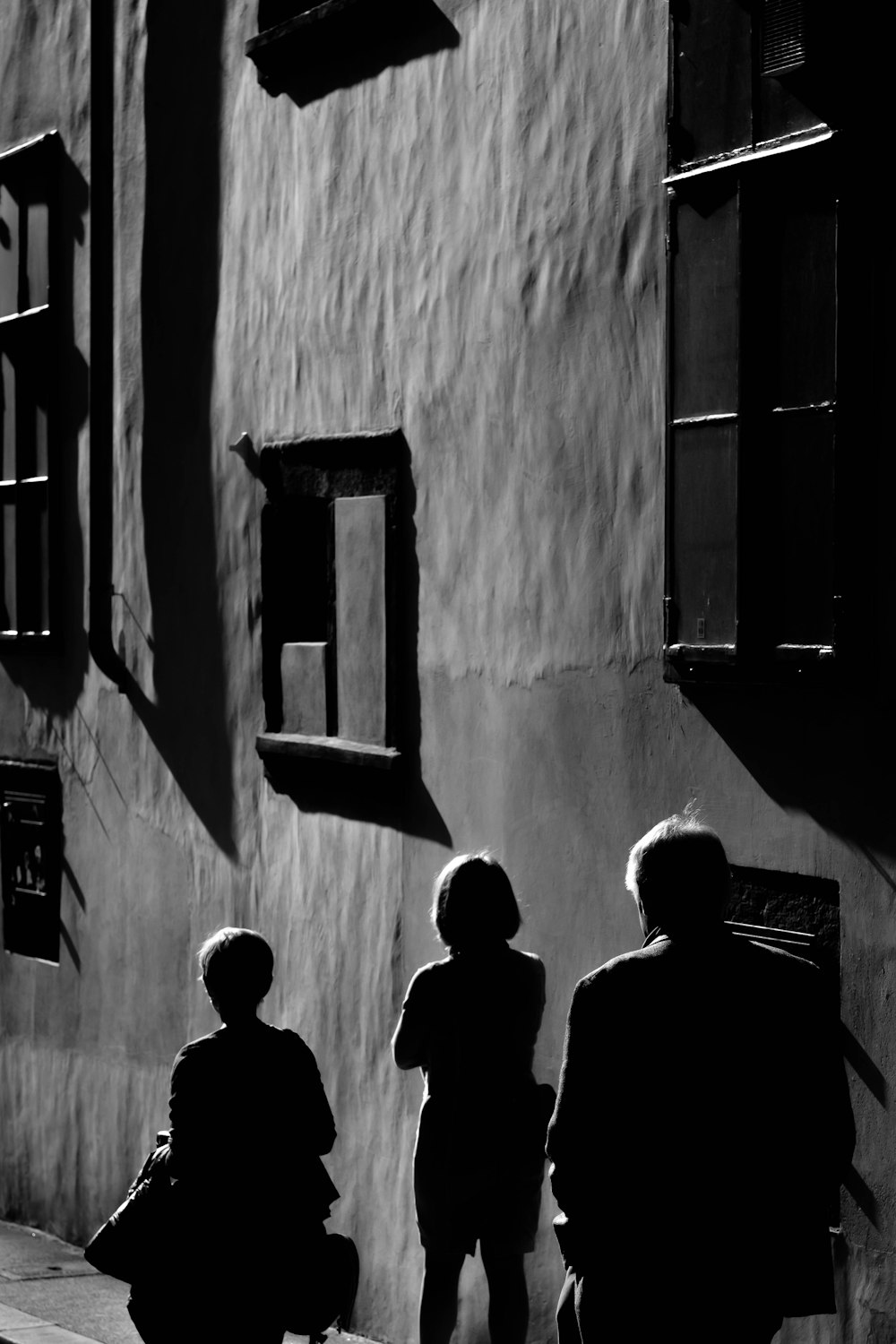 three persons walking near gray wall