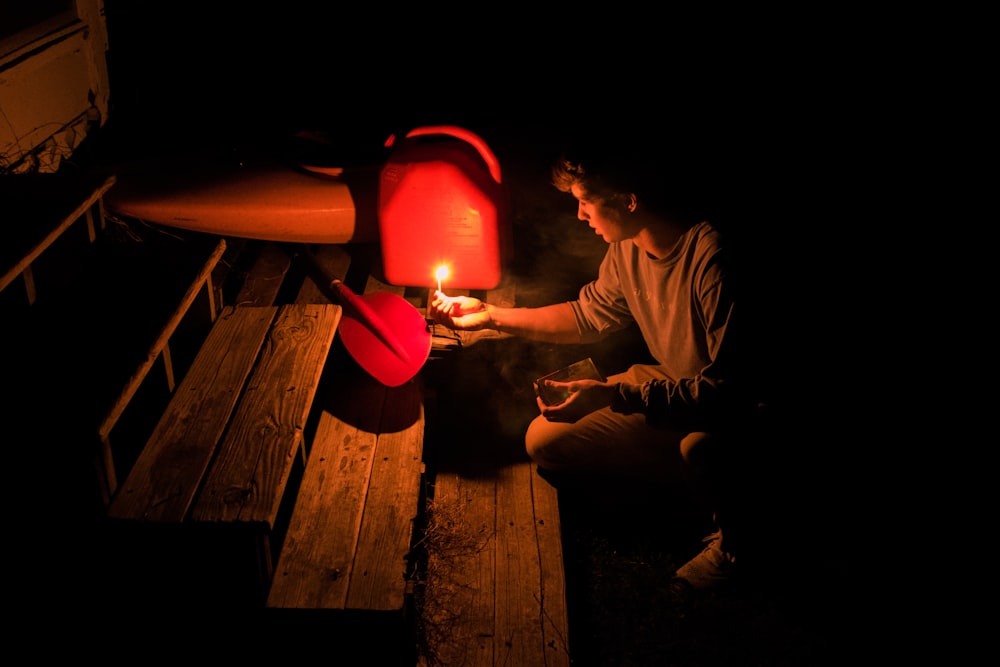 person holding candle lighting the red and black metal part in dark room near ladder