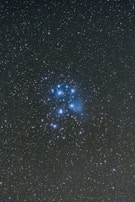 A starry sky featuring a cluster of bright blue stars surrounded by numerous smaller stars scattered across the dark, expansive space.