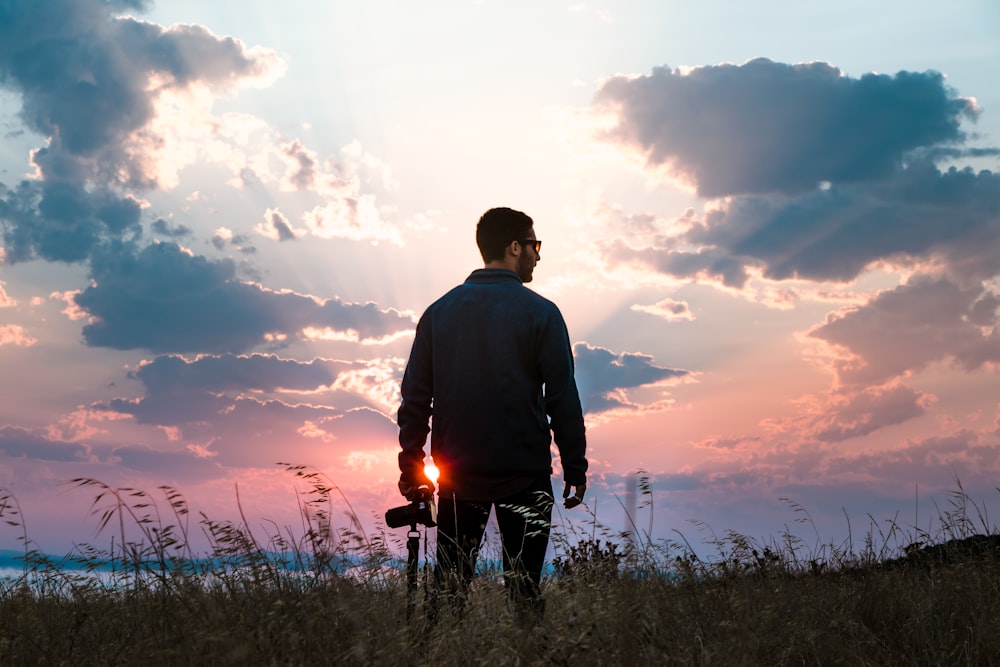 man in black long-sleeved shirt holding DSLR camera standing on grass