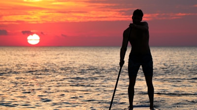 man riding paddleboard silhouette during golden hour