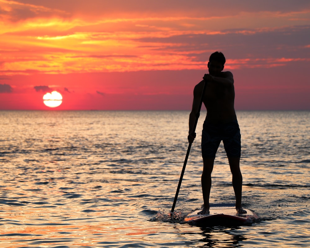 Mann reitet Paddleboard-Silhouette während der goldenen Stunde