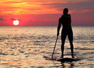 man riding paddleboard silhouette during golden hour