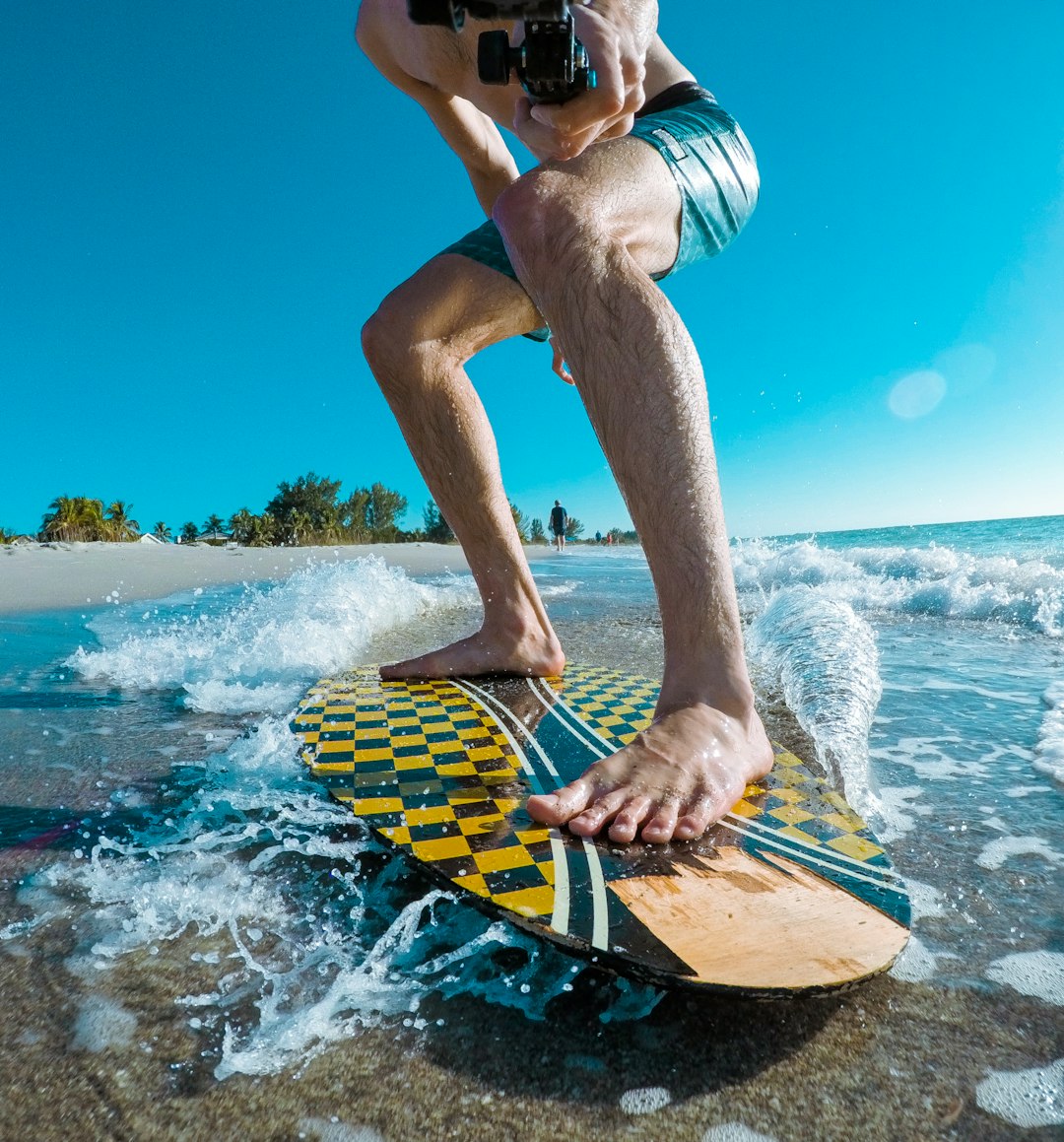 person surfboarding while taking footage of himself on beach during daytime