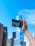 Close-up of a smiling travel influencer holding a sleek camera with a cityscape background.