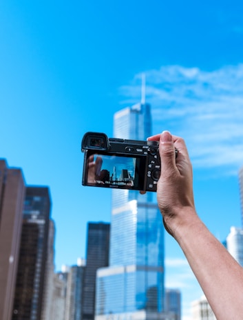 Close-up of hand holding a camera capturing a city skyline.