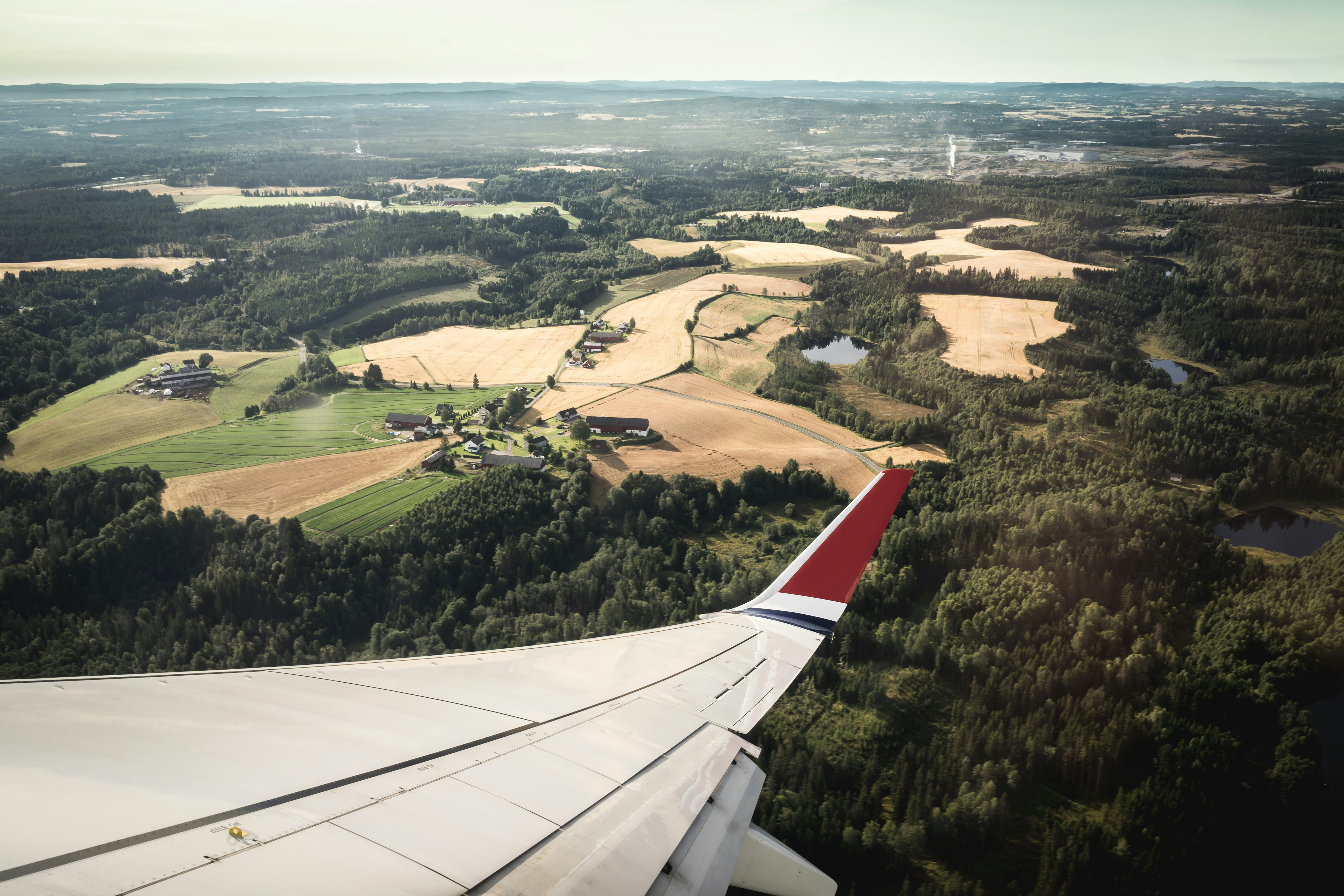 white and red airplane wing in distance brown field and green leafed trees at daytime